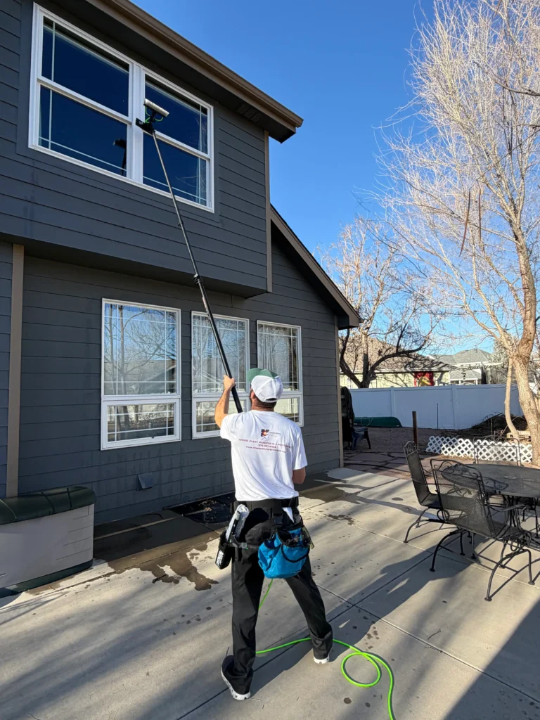 Side view of window cleaner extending water-fed pole to second-story window.